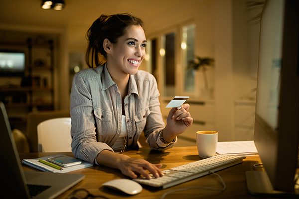 Young happy woman using credit card for online shopping in the evening at home.